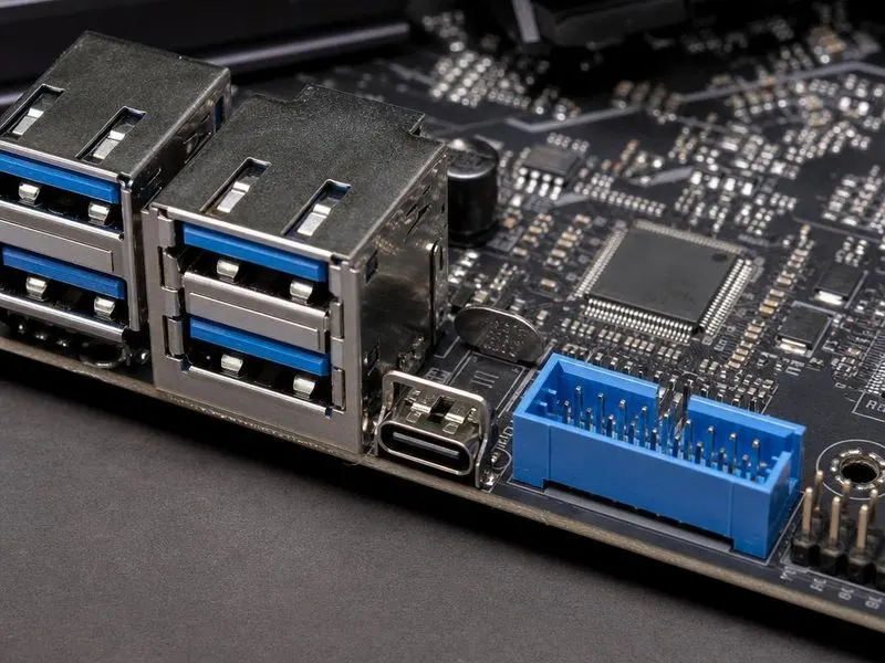 Real hardware teardown of desktop motherboard USB controller section with rear USB-A and USB-C ports, blue USB 3 internal header, USB 2 header pins, host-controller IC, port power switches